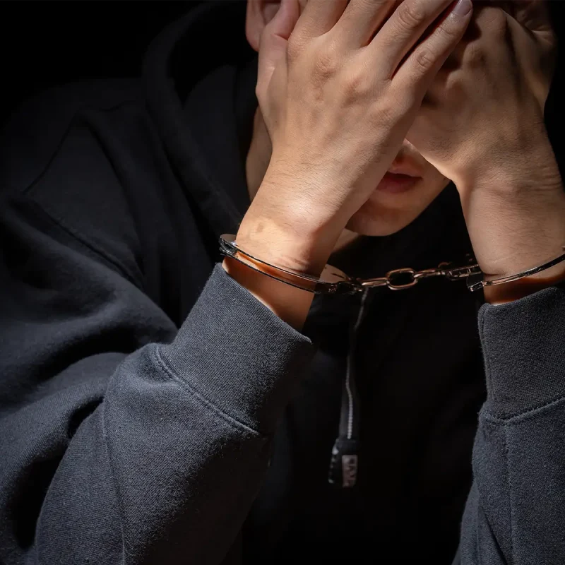 close-up of a man wearing handcuffs with his hands covering his face