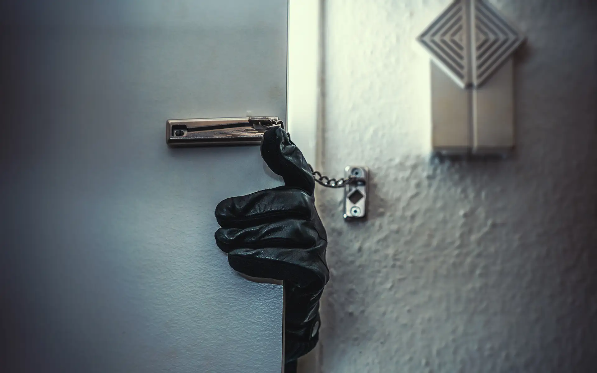 A burglar's gloved hand opening the door of a house