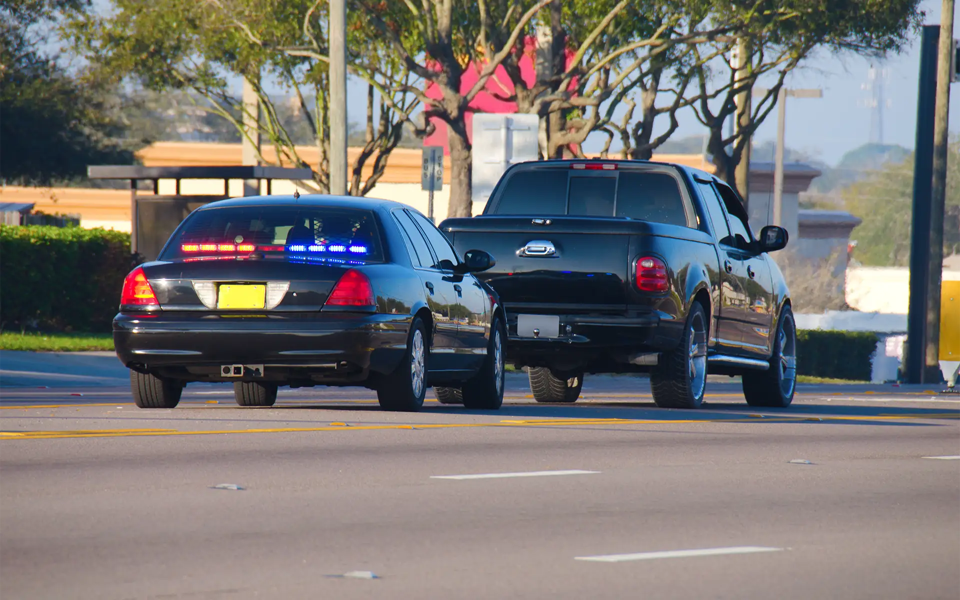 The rear view of an unmarked police car pulling over a black truck for driving with a suspended license